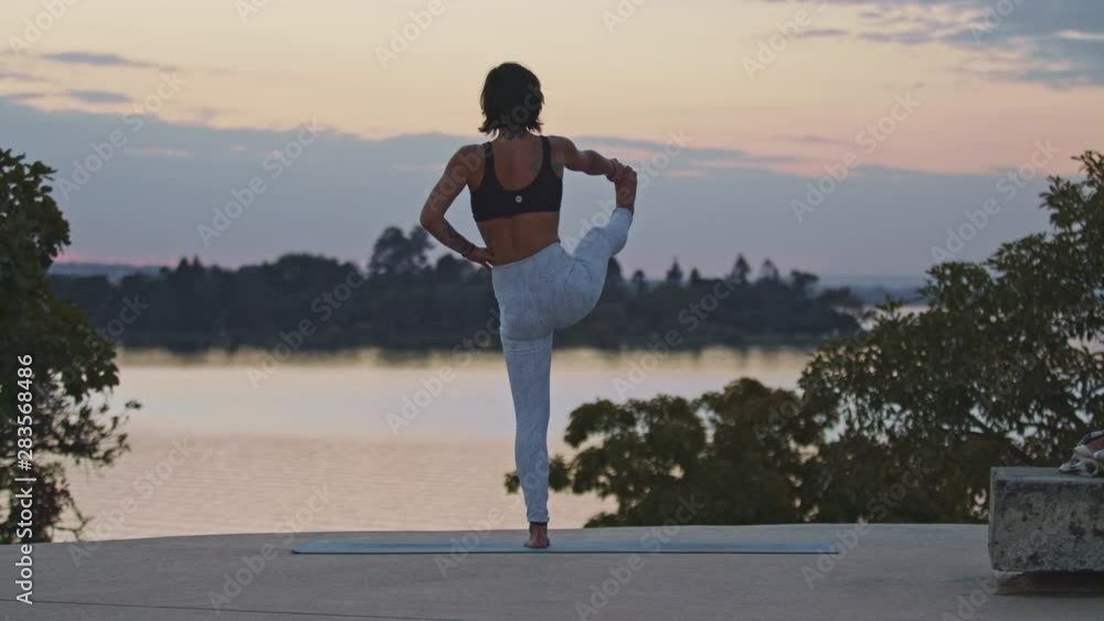 Young flexible woman holds her foot while standing in a yoga pose. Outdoor scene. Young flexible woman holds her foot while standing in a yoga pose. Outdoor scene.