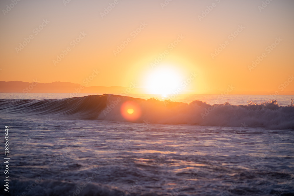 Landscape shot of waves crashing with bright sun rising over the horizon in background