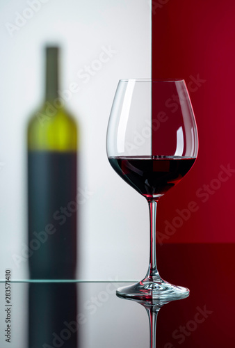 Bottle and glass of red wine on a black reflective background.