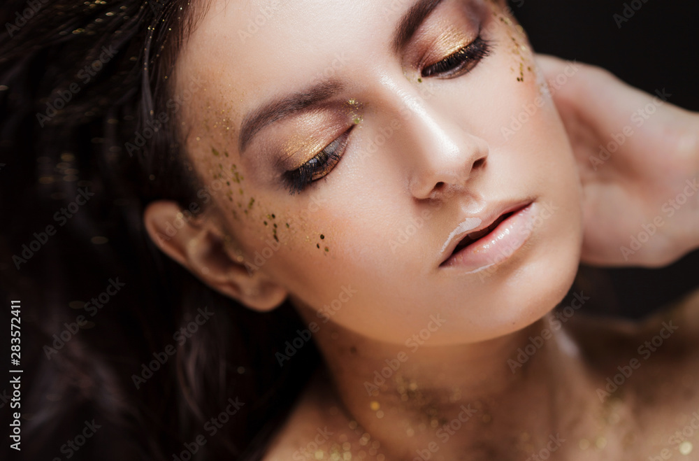Charming girl with trendy glitter makeup, fashionable make-up with gold glitter on the cheekbones and near the eyes. Charming girl with trendy glitter makeup, fashionable make-up with gold glitter on the cheekbones and near the eyes.