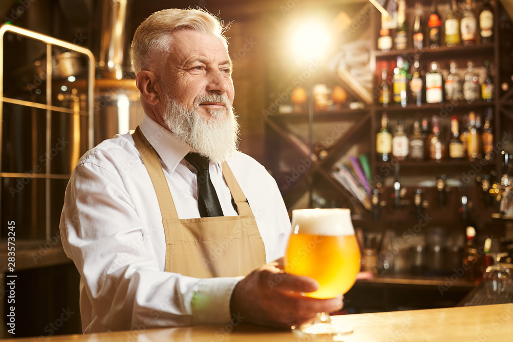Brewer standing over bar and keeping glass of golden beer Brewer standing over bar and keeping glass of golden beer