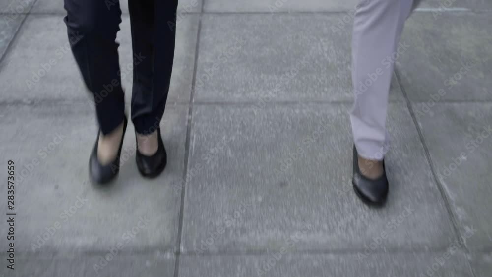Legs of businesswomen walking on street. Low section of young female colleagues in formal wear walking together outdoor. Business concept Legs of businesswomen walking on street. Low section of young female colleagues in formal wear walking together outdoor. Business concept