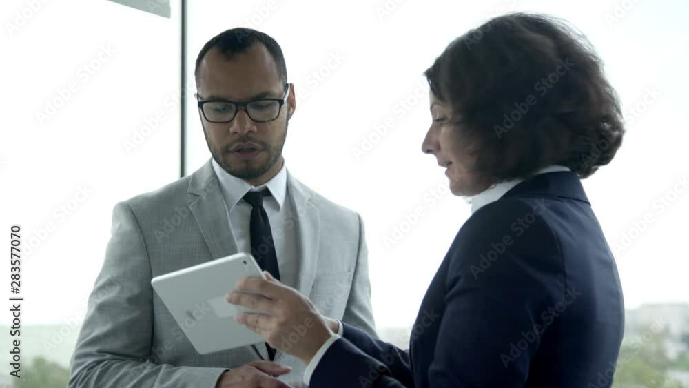 Focused colleagues looking at tablet and talking. Two confident business people discussing some questions. Business meeting concept Focused colleagues looking at tablet and talking. Two confident business people discussing some questions. Business meeting concept