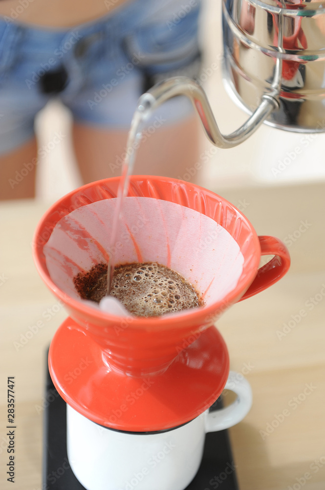 Girl barista brews coffee drip method. Pouring water from gooseneck kettle into red hario v60 funnel. Girl barista brews coffee drip method. Pouring water from gooseneck kettle into red hario v60 funnel.