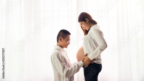 Asian man husband hugging pregnant wife and happiness together at home. Pregnancy and family concept.