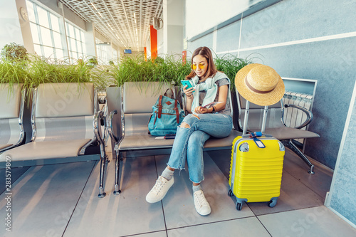 Young asian woman passenger uising smartphone while waiting and sitting in airport or train station terminal hall