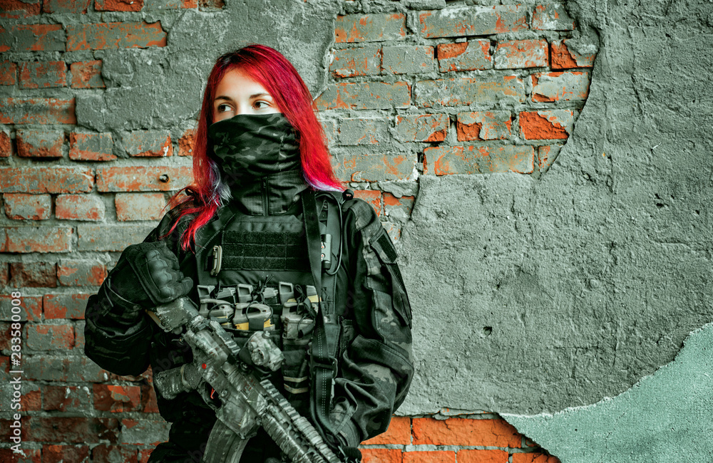 Airsoft red-hair woman in uniform with machine gun beside brick wall ...