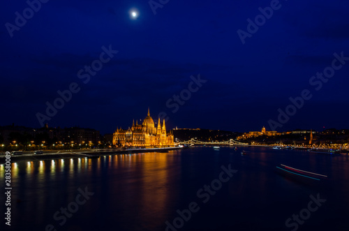 Nightscape city view of Budapest parliament under the cloud covered moon in the sky and water reflection © Souvik
