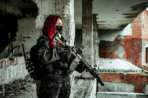 Airsoft red-head woman in uniform and put down machine gun. Soldier standing on balkony. Horizontal photo side view