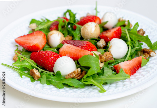 Salad with mozzarella cheese, arugula and strawberries on a white plate. Healthy summer green salad for diet, snack or light dinner.