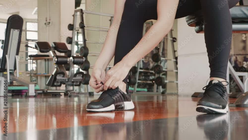 Close up of young sport woman tie up training shoe shoelace rope in fitness gym. Healthy and people lifestyle concept. Relaxation and cooling down after workout with club background. Slow motion HD Close up of young sport woman tie up training shoe shoelace rope in fitness gym. Healthy and people lifestyle concept. Relaxation and cooling down after workout with club background. Slow motion HD