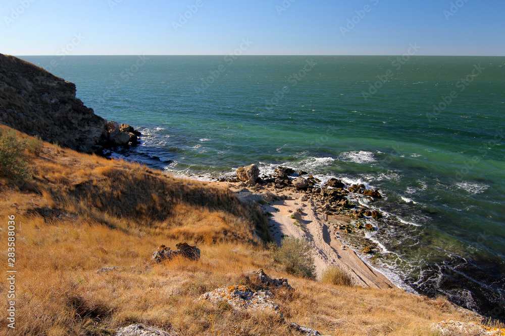 Secluded sandy beach with turquoise sea in the foreground yellow grass and stones