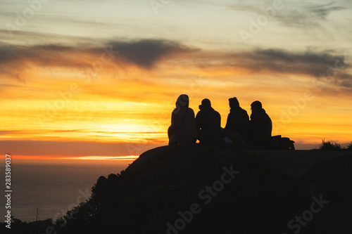 Silhouettes of friends travelers on top of a hill watching a beautiful sunset and talking, California