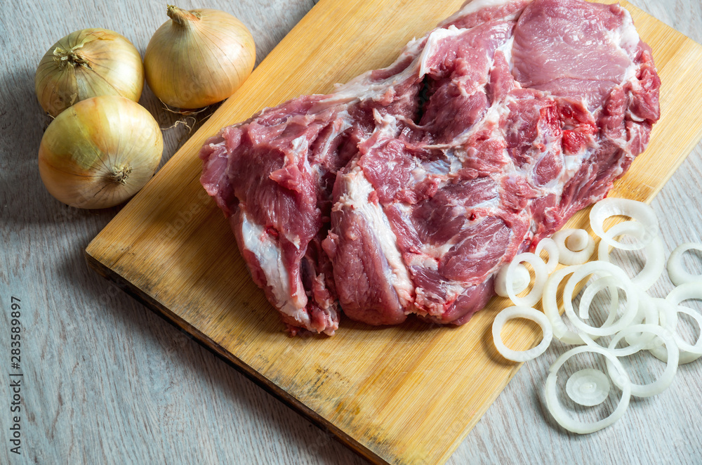 Raw meat and onion rings on wooden board Raw meat and onion rings on wooden board
