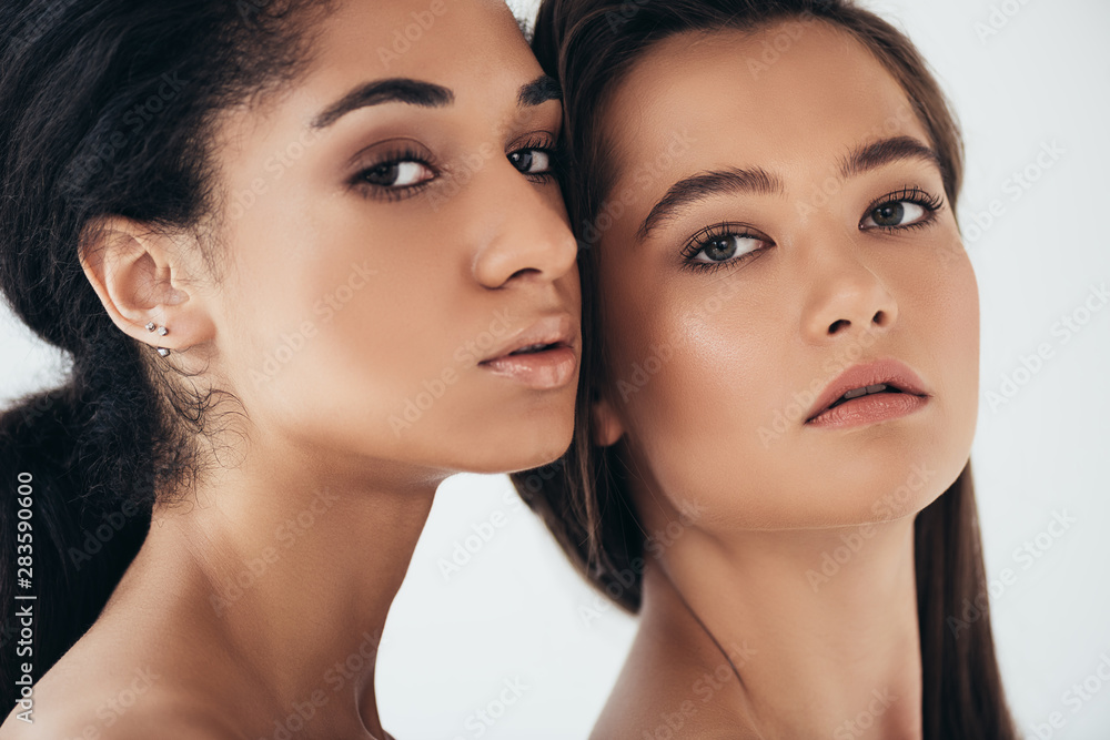 two attractive multiethnic young women looking at camera isolated on grey