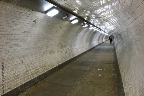 Interior of Greenwich foot tunnel that connects both sides of London under river Thames  lit by neon lights  wide angle photo with blurred pedestrians in distance