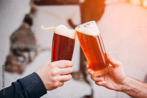 Two mans hands with glass of beer toasting creating splash 