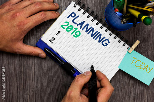 Conceptual hand writing showing Planning 2019. Business photo showcasing Begin with end in the Mind Positioning Long term Objectives Man holding marker notebook reminder cup markers wood table