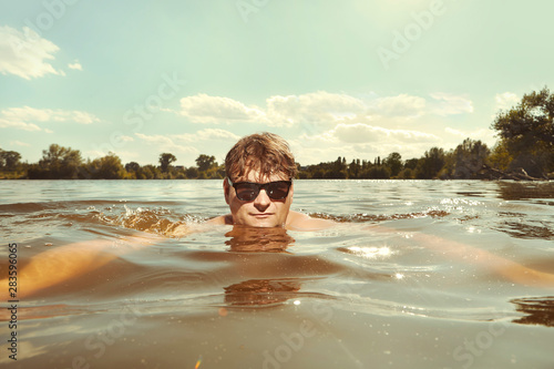 Funny man in sunglasses swimming in lake on inner tube
