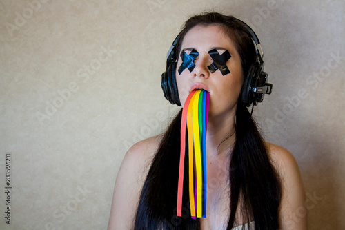 Young woman with sealed eyes, in headphones and with a flowing rainbow from her mouth