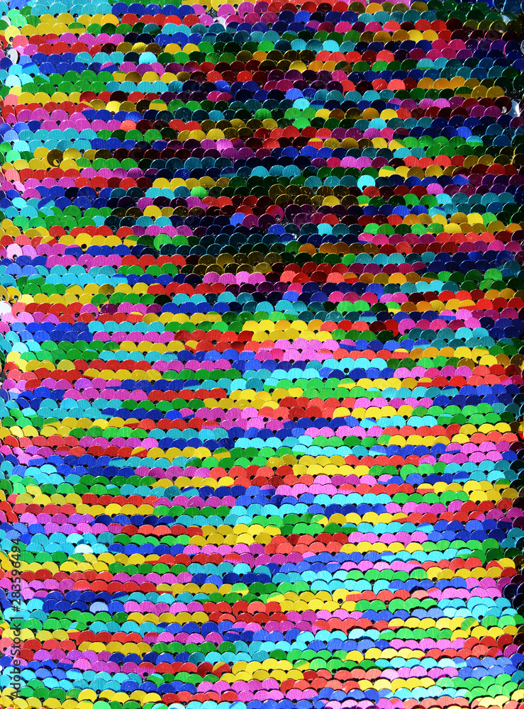 Sequins close-up macro. Abstract background with multicolor sequins on the fabric. Texture scales of round rainbow sequins with color transition.