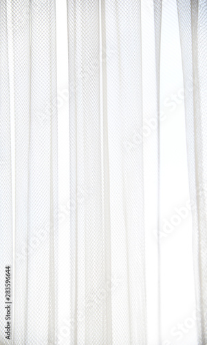 White tulle curtain with vertical folds. Window with light curtains. Soft textile texture. Light and shadow abstract background.