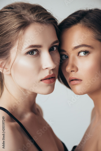 two attractive young women looking at camera isolated on grey