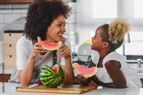 Beautiful African Mother and Daughter eating Watermelon at Home Kitchen photo