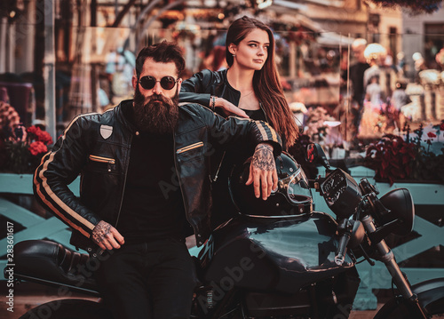 Beautiful couple with brutal biker and his sexy gilfriend are chilling near cefeteria with motorbike. photo
