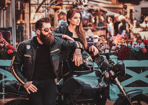 Beautiful couple with brutal biker and his sexy gilfriend are chilling near cefeteria with motorbike. photo