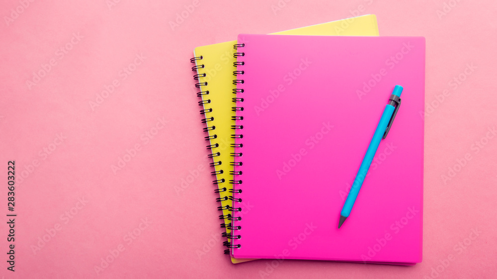 two Notepads pink and yellow with blue pen on a pink background. Place for text. Note Sheet two Notepads pink and yellow with blue pen on a pink background. Place for text. Note Sheet