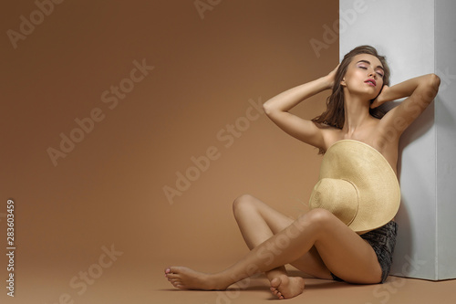 beautiful sexy woman with sun hat is sitting relaxed. Full length studio shot