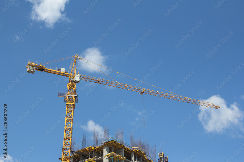 The structure of a house under construction against a blue sky. The work of a tower crane during the construction of the building on a sunny day. Monolithic construction of buildings.