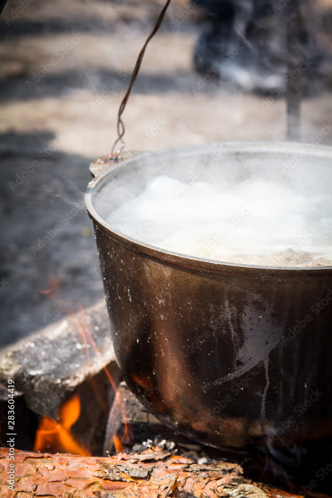 The concept of camping kitchen, on a tripod over a fire there is a pot in which food is prepared, selective focus