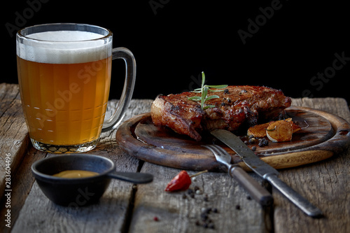 Still life with a big fried steak, a glass of beer, mustard and cutlery on an old wooden tabletop, the concept of Oktoberfest and St. Patrick's Day