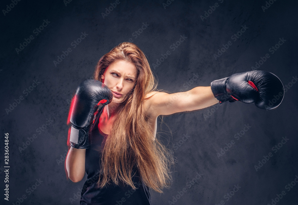 Beautiful woman with long hair is demonstraiting her hit at studio. She is wearing boxing gloves.