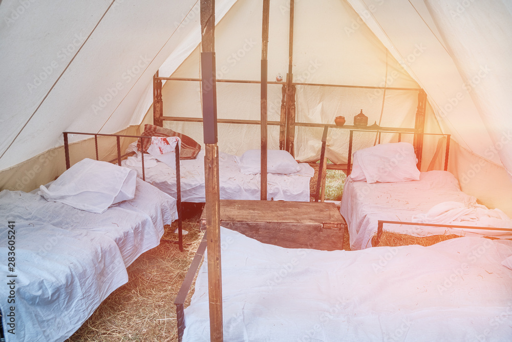 Beds under a large tent retro field hospital. Military field medicine in the 18th or 19th century. Portable hospital for wounded soldiers. Beds under a large tent retro field hospital. Military field medicine in the 18th or 19th century. Portable hospital for wounded soldiers.