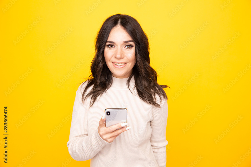 Smiling pretty woman with phone standing isolated on the yellow background Smiling pretty woman with phone standing isolated on the yellow background