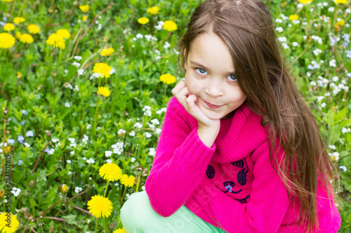 Cute little girl is sitting in a field with dandelions.