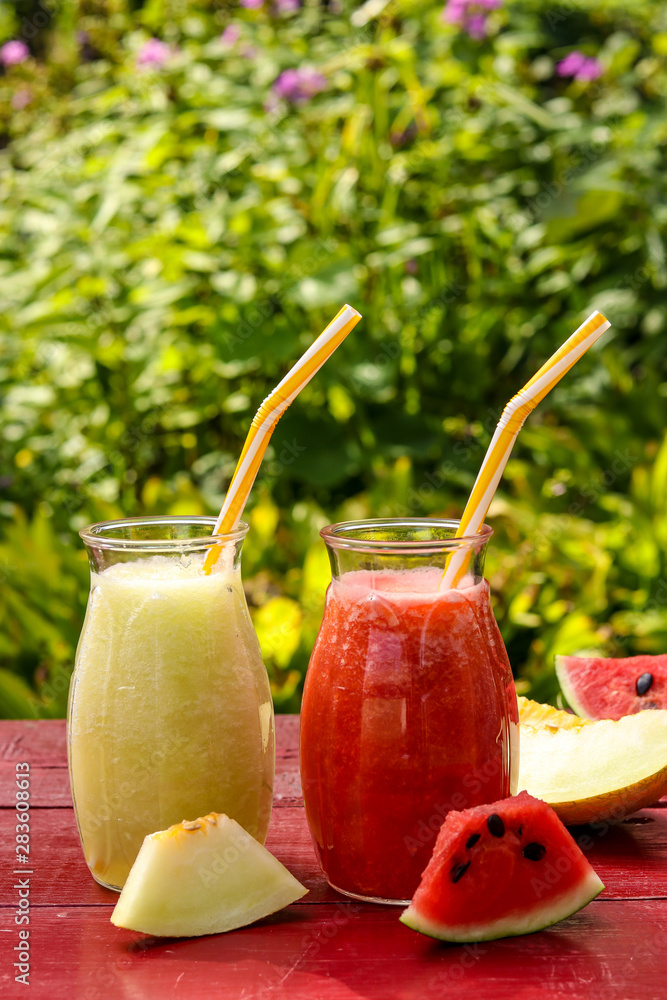 Homemade fruit smoothies made of watermelon and melon on a table in the garden, vertical orientation Homemade fruit smoothies made of watermelon and melon on a table in the garden, vertical orientation