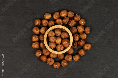 Lot of whole ripe brown hazelnut in circle in tiny wooden bowl flatlay on grey stone