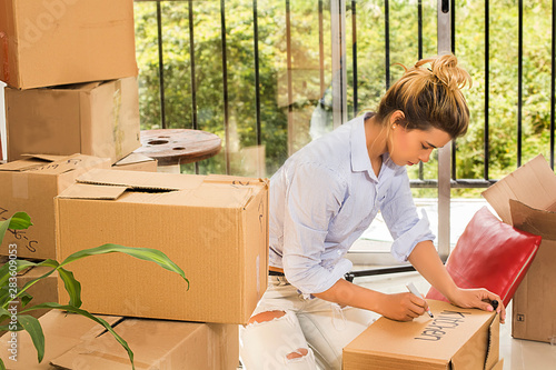 Young woman kneeling marking the cardboard boxes with her belongings for her transfer.