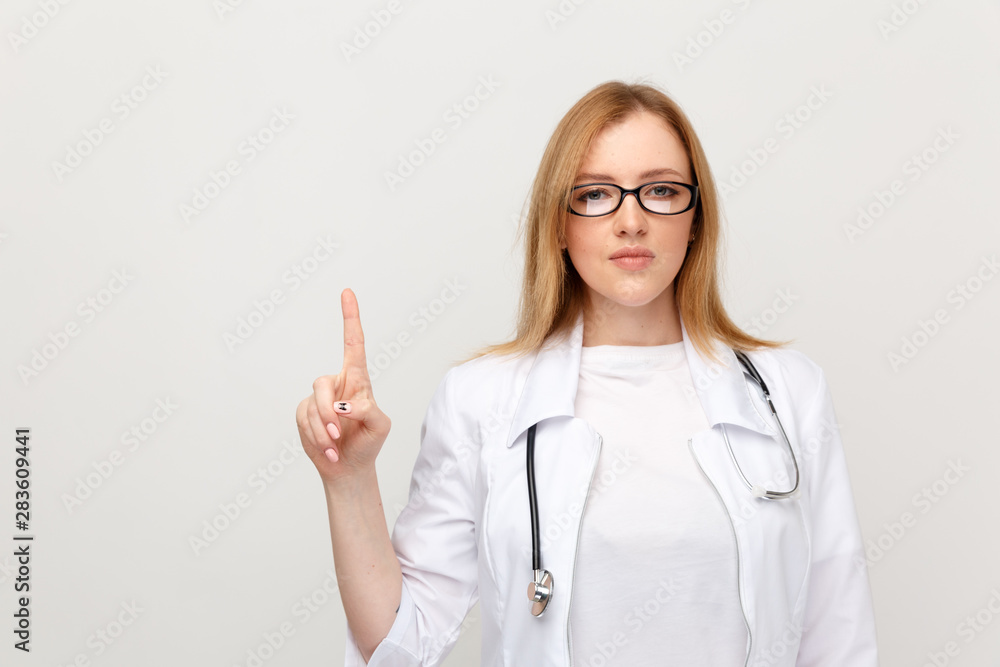 Female doctor in glasses pointing by finger standing in the white studio Female doctor in glasses pointing by finger standing in the white studio
