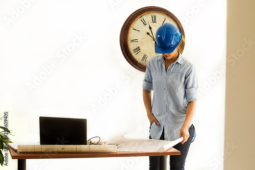 Female architect looking at blueprints of construction drawings in her office with her safety helmet