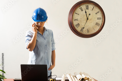 Female architect looking at blueprints in her office and talking on cellphone