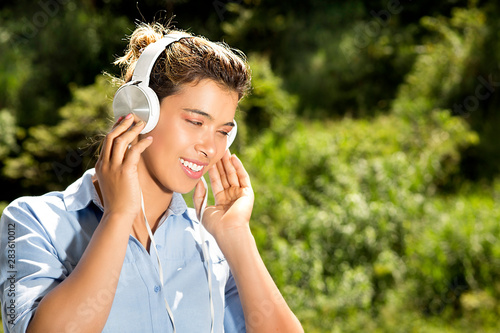 Young woman listening to music from the headphones. Against background of green grove isolated. Beautiful female model.