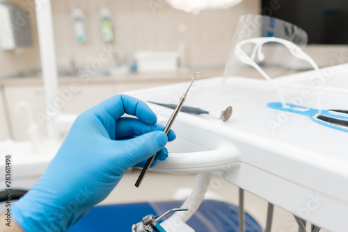 The hand of the dentist in the glove holds tool probe. . Stomatological instrument in the dentist clinic. Dental work in clinic. Office where dentist conducts inspection and concludes.