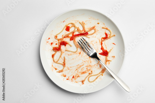 Dirty plate with food leftovers and fork on white background, top view