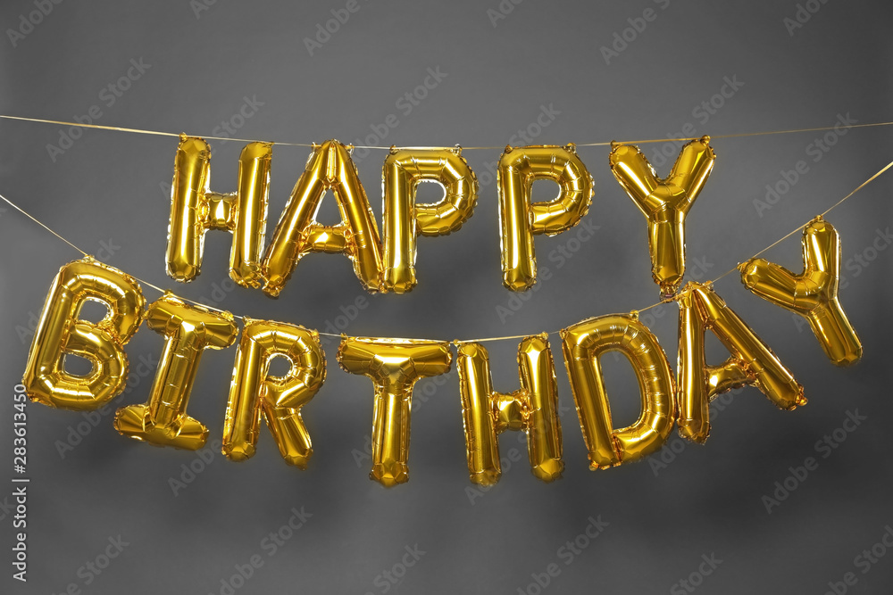 Phrase HAPPY BIRTHDAY made of golden balloon letters on grey background