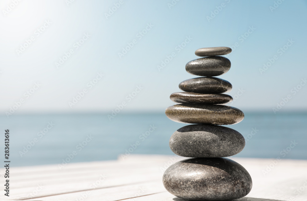 Stack of stones on wooden pier near sea, space for text. Zen concept - obrazy, fototapety, plakaty 